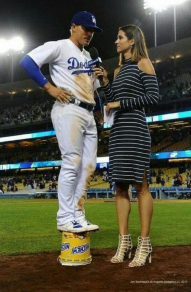 baseball player standing on bucket talking to tall reporter